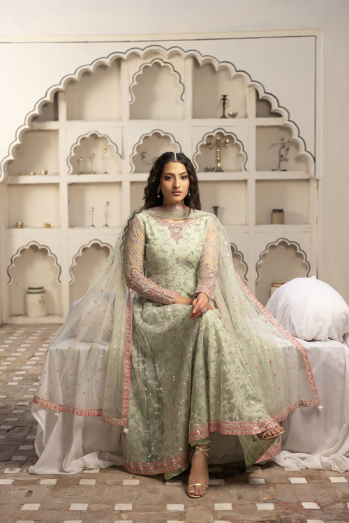 Woman in a light green traditional outfit sitting in a decorative room.
