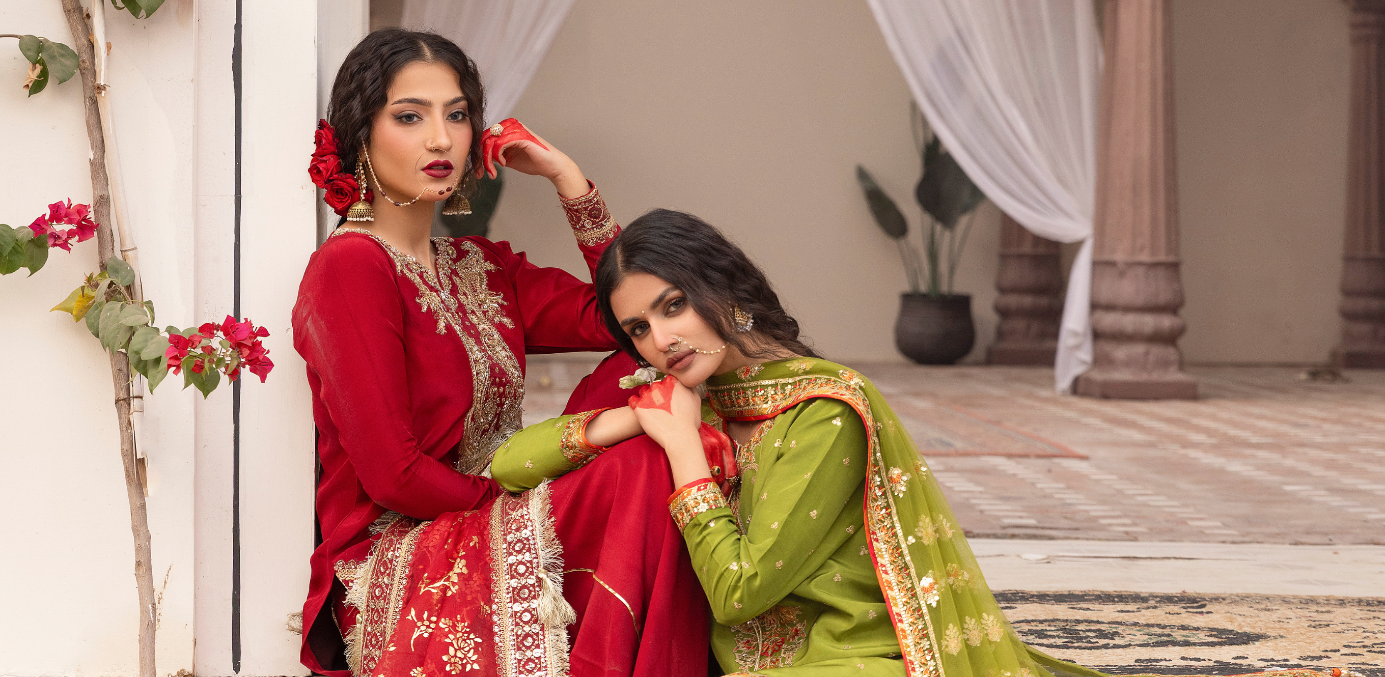 Two women in traditional red and green dresses sitting on a step.